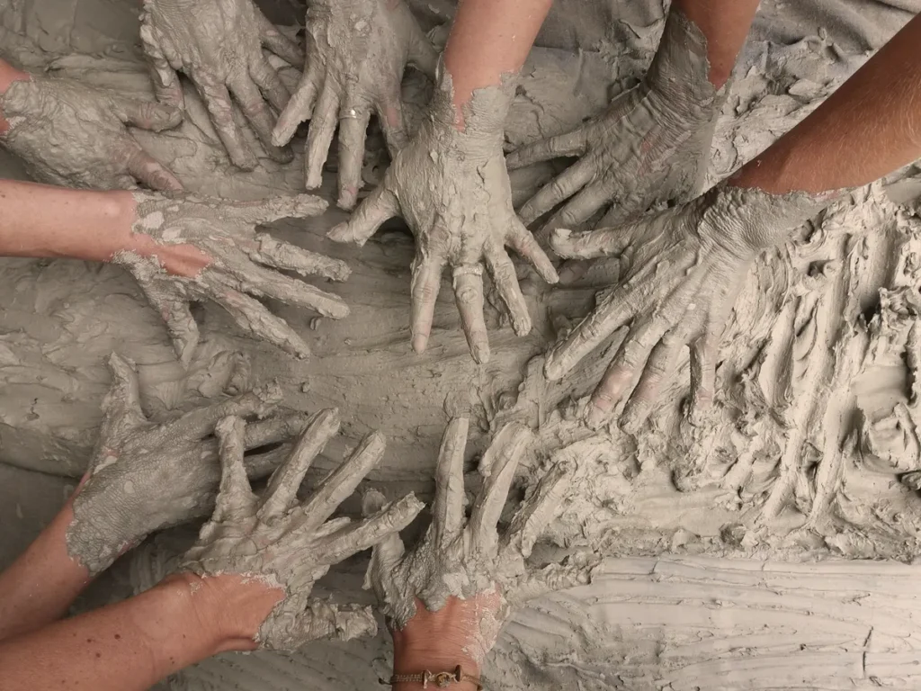 Many hands shaping clay together, honoring the sacred connection to Earth and the collective Homecoming to our roots